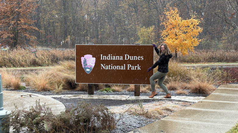 A young woman poses with the Indiana Dunes National Park sign in a snowstorm.