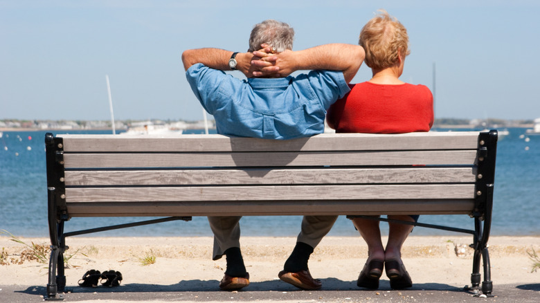A senior couple relaxes on a bench by a Cape Cod beach