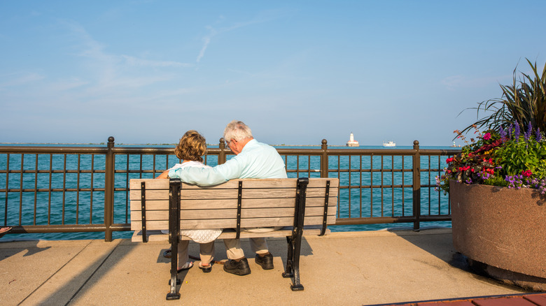 An elder couple sit on park bench near water