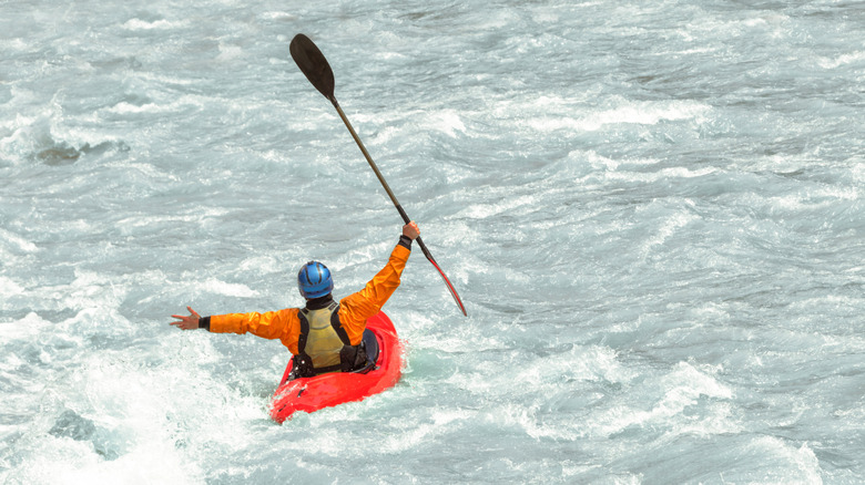 Man whitewater kayaking through rapids from behind