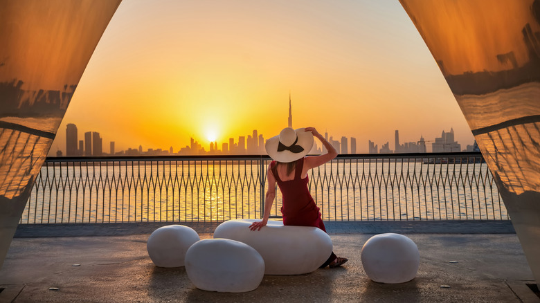 Woman with hat sitting on large stones overlooking cityscape in Dubai and ocean
