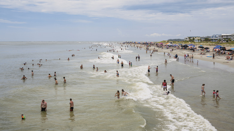 A crowded day on the water at Tybee Island in Georgia with people swimming in the water and umbrellas set up on shore