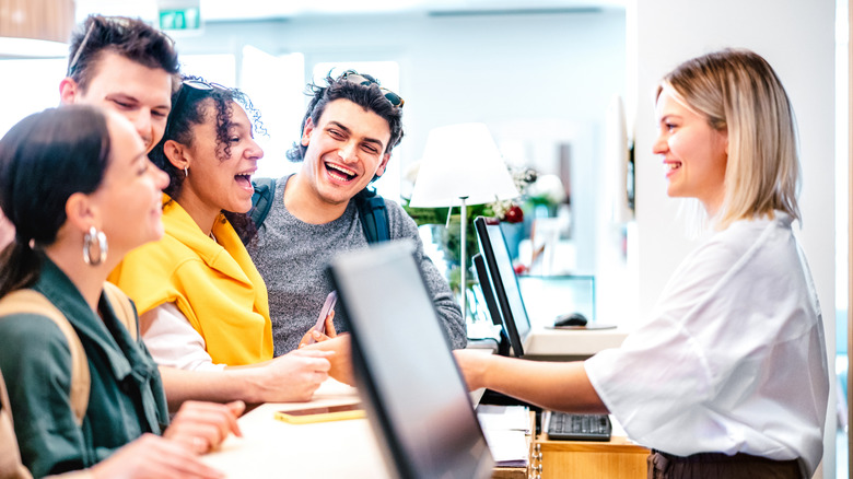 Four young travelers smiling and talking to a hotel front desk hostess behind a counter