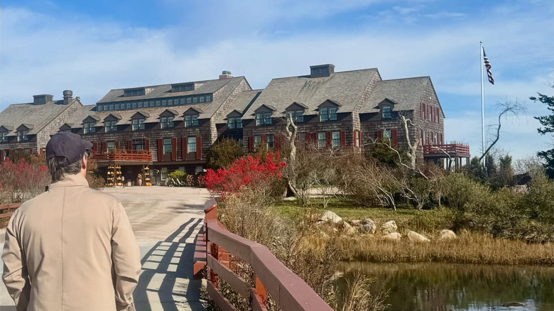 Person walks along a pathway beside a red wooden railing, approaching the historic Weekapaug Inn in Rhode Island