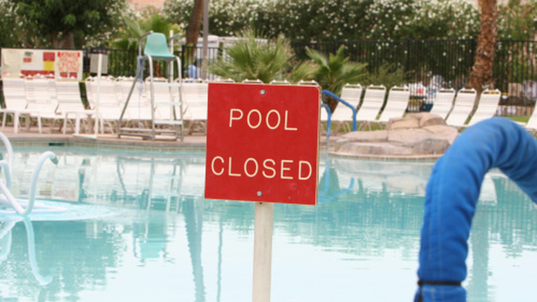 Red "Pool Closed" sign against a swimming pool in a resort