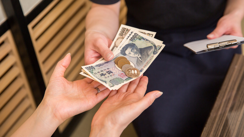 A waiter's hand holding a clipboard and returning Japanese yen bills to a customer