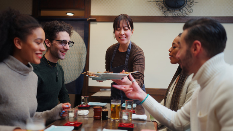Smiling server serving small plates of food to a group of diners in a restaurant