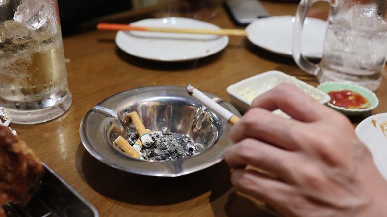 Close-up of cigarette and ashtray on a table with beer glasses, plates, and chopsticks