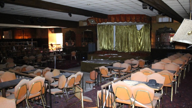 Abandoned ballroom with gold stage and overturned chairs