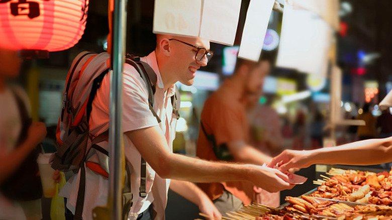 A vendor off-frame handing change to a Western tourist in a Japanese street food stall