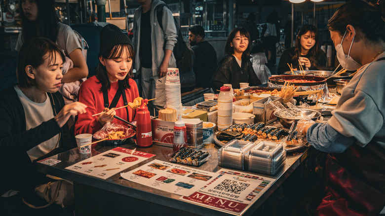 A group of female diners eating street food on a table filled with meals and menus