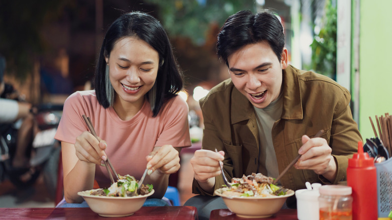 Couple digging into bowls of pho with spoons and chopsticks