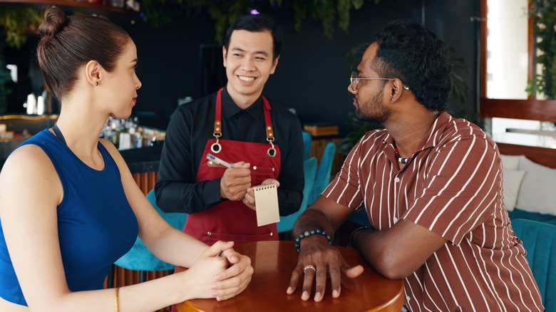 Smiling Asian waiter takes a young couple's food orders