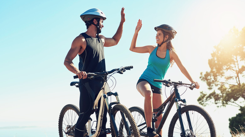 A man and woman high-five from the saddles of their mountain bikes