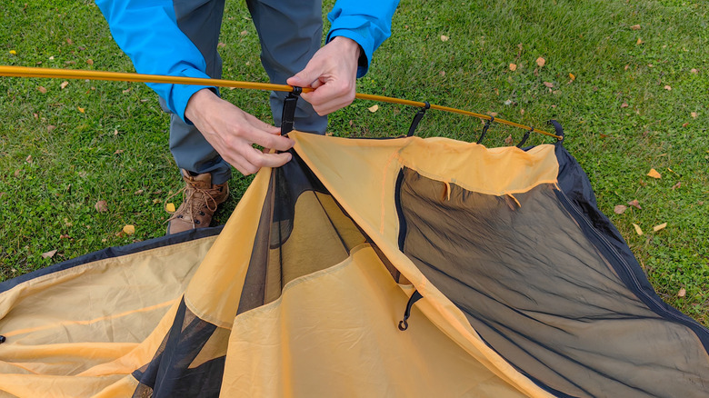 A person in a blue jacket setting up a brown tent