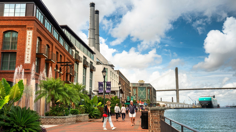 Pedestrians walking past buildings along the riverfront in Savannah