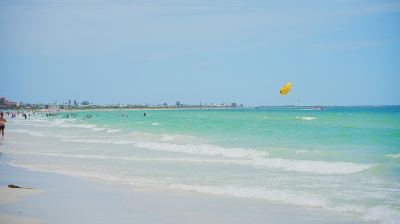 blue ocean water by beach with yellow parasail in background