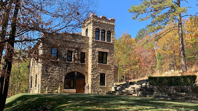 A stone castle standing against trees with green and red leaves and blue skies