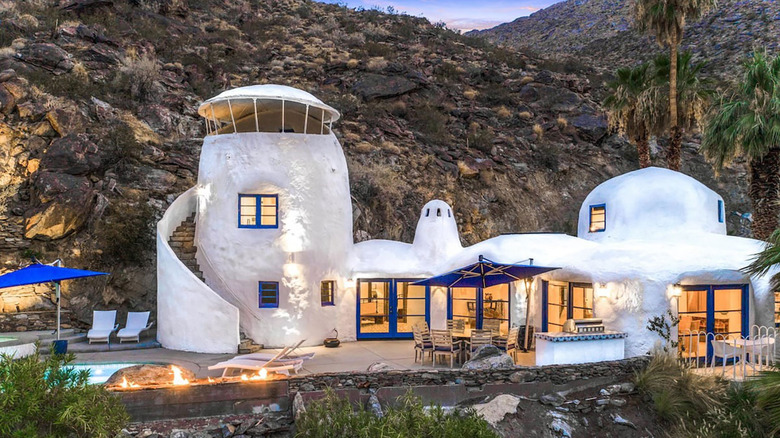 Curved white stucco volumes with blue shuttered windows, framed against a mountain backdrop
