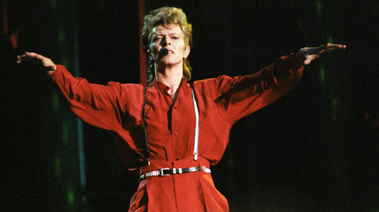 David Bowie performing on stage in London wearing red shirt and trousers with suspenders