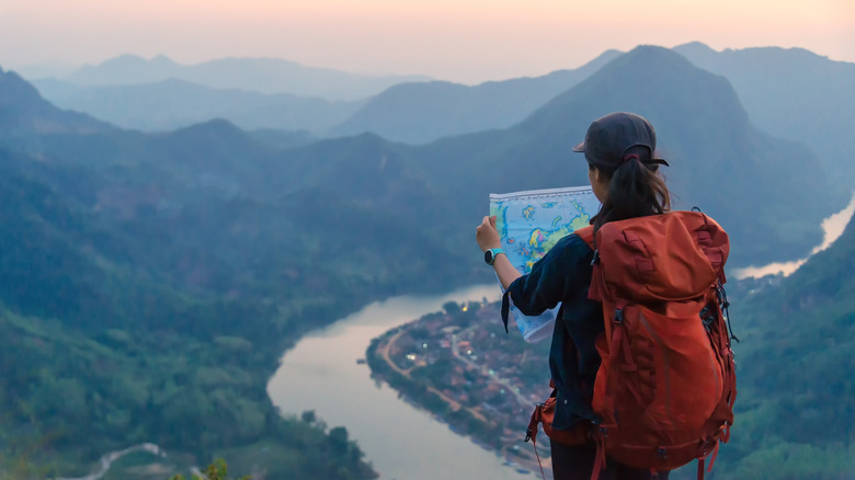A hiker with red backpack consulting a map in a Laos mountain