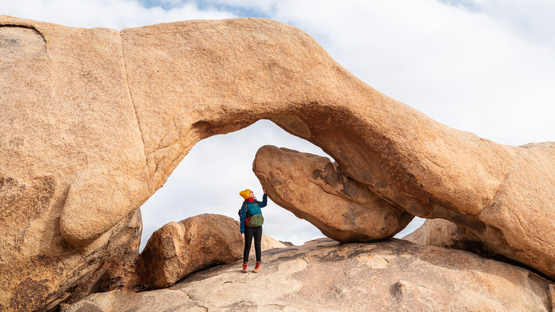 Woman hiking under Arch Rock in Joshua Tree National Park, California