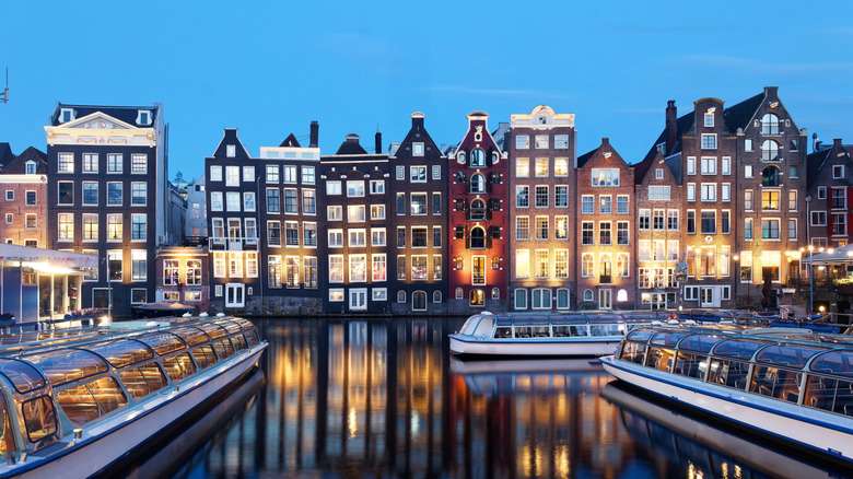 A canal in Amsterdam at dusk, with boats and row houses