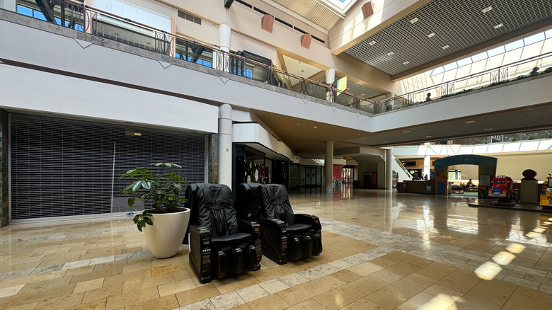 Black massage chairs beside a plant in an empty mall, with two levels of closed stores in the background