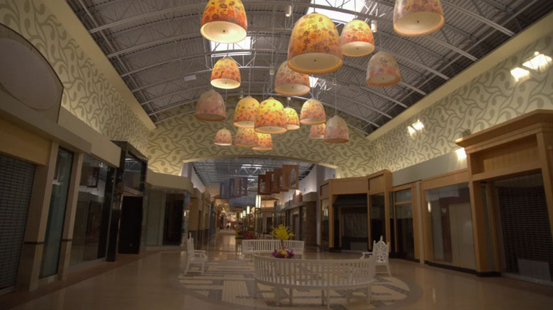 Empty hallway at Pittsburgh Mills Mall, with white benches under yellow light fixtures and empty storefronts to either side