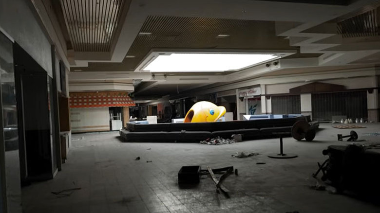 Large yellow fish play equipment surrounded by closed stores and debris under a skylight in the Pines Mall