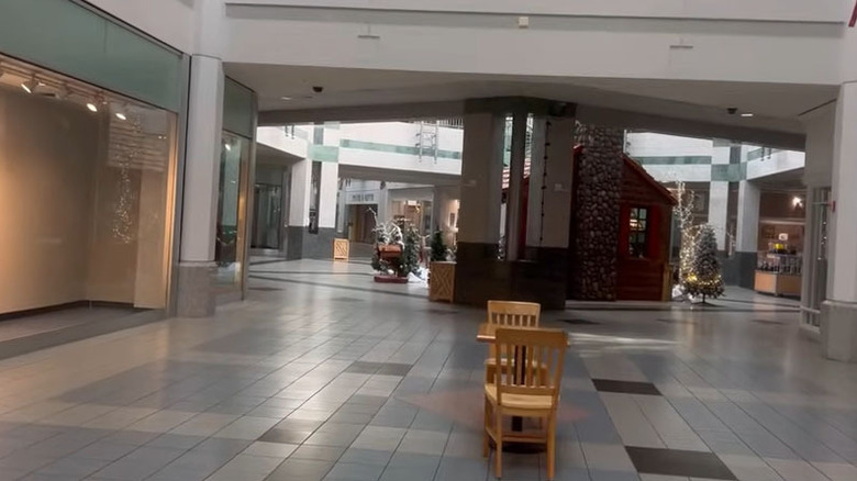 View of The Vista's empty hallways, with a wooden table in the foreground and a fake log cabin Christmas display in a white-walled mall hallway