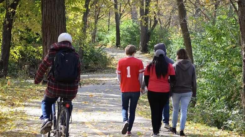 Biker in a plaid jacket passes four people walking in red and gray shirts, on a trail of the Central Ohio Greenways