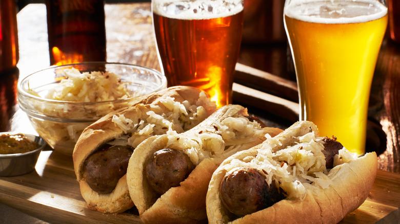 A closeup of German bratwursts on buns with sauerkraut served with beer