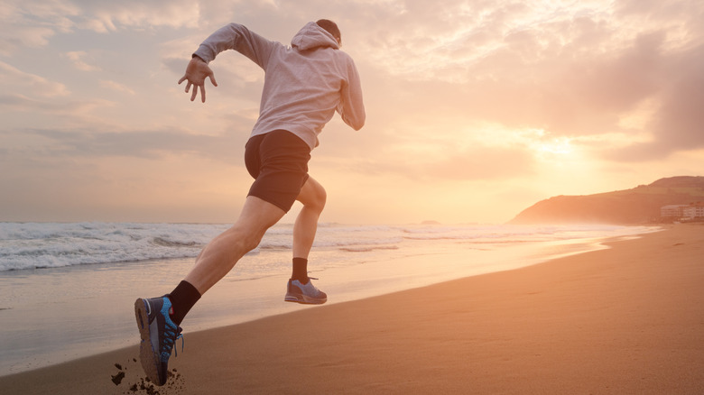 A man sprinting through the surf on a beach, seen from behind