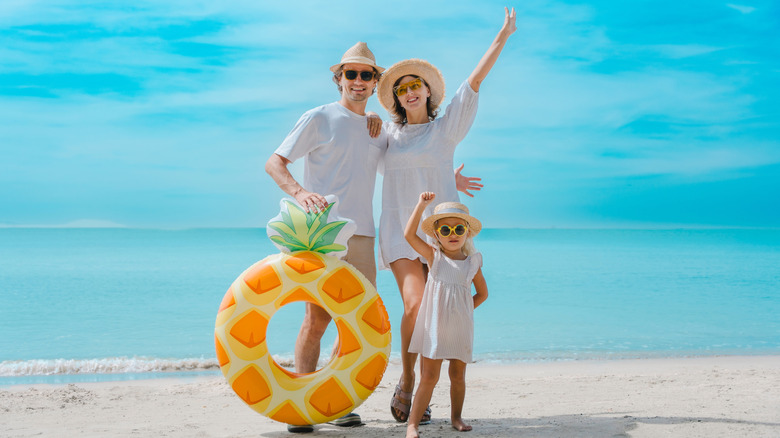 A mom, dad and young daughter standing on a tropical beach and smiling