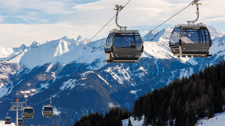 A cable car dangles over snow-covered mountains