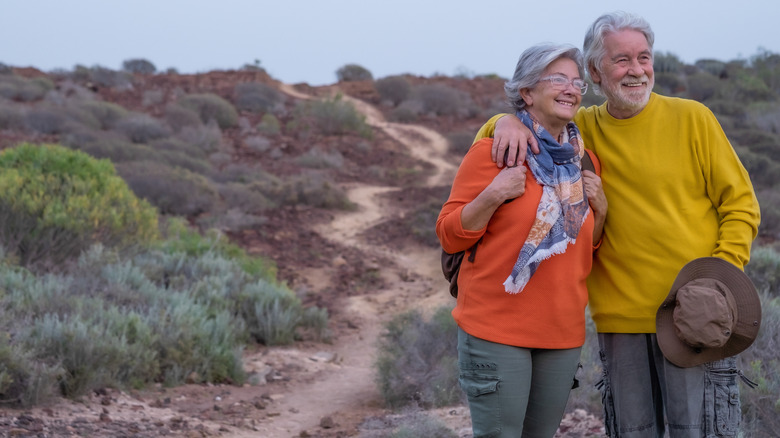 A retired couple standing together smiling on a desert hiking trail in California