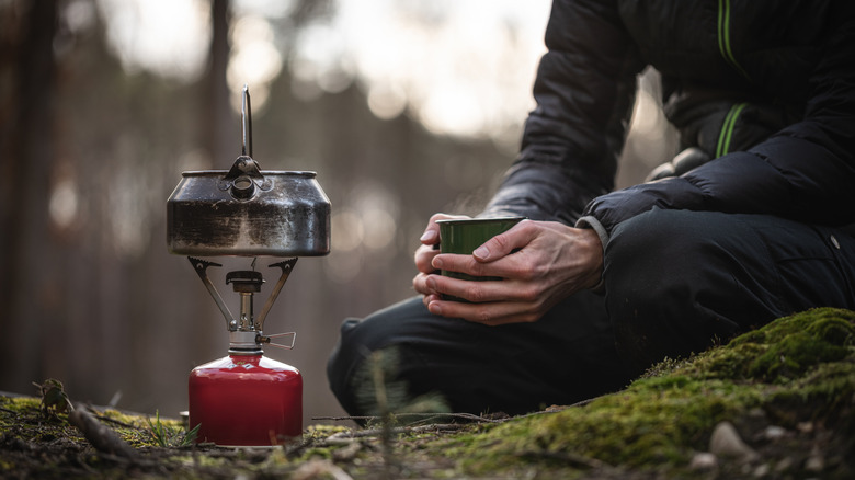 Camper clutching a cup near a portable camping stove