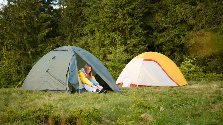 Woman sitting in a tent's entrance next to another tent