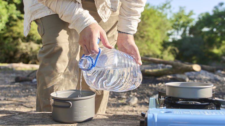 Person pouring water into a pot next to a camp stove
