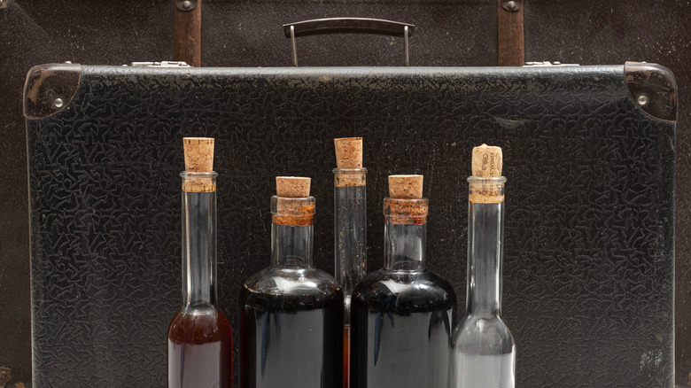 Five corked bottles filled with liquid in front of a suitcase