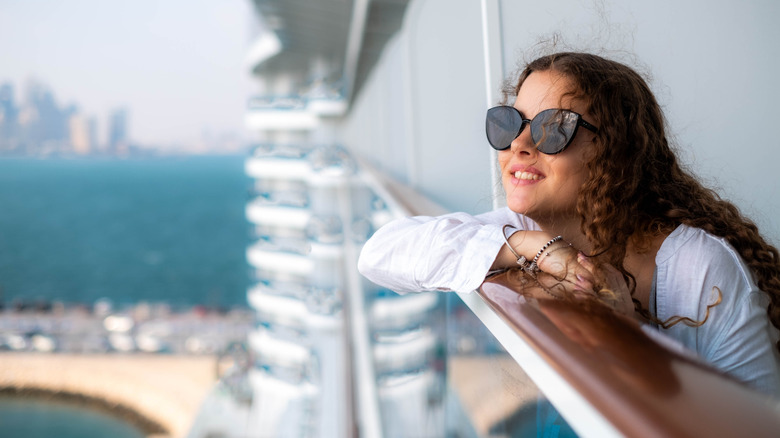 A young woman in sunglasses leaning on the balcony railing of a cruise ship