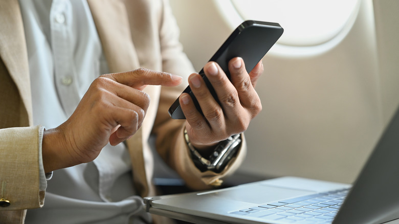 Airplane passenger holding a phone with a laptop on their tray table