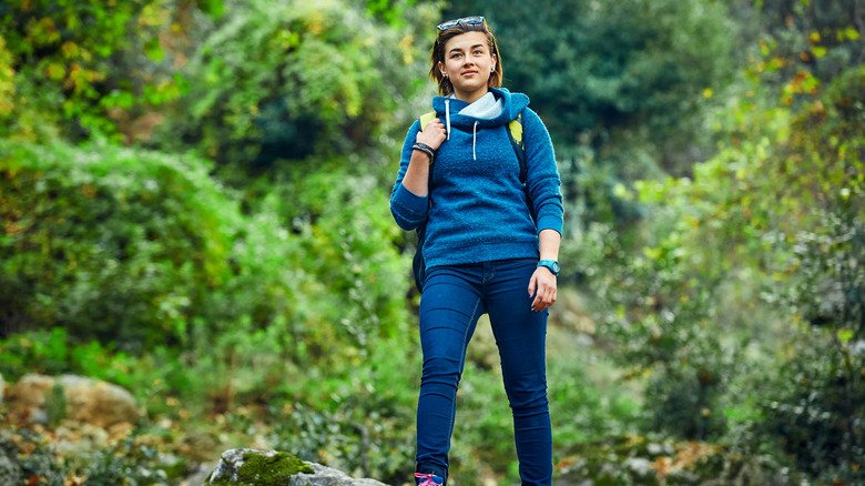 A hiker wears blue jeans and sweatshirt in the woods