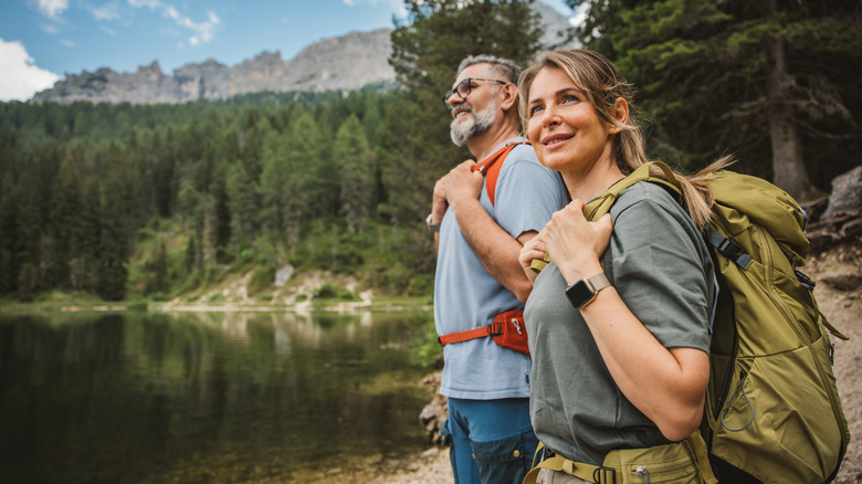 A pair of middle-aged hikers stands on the edge of a wooded lake