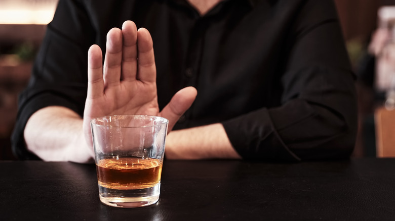 Man's raised hand refusing glass of alcohol