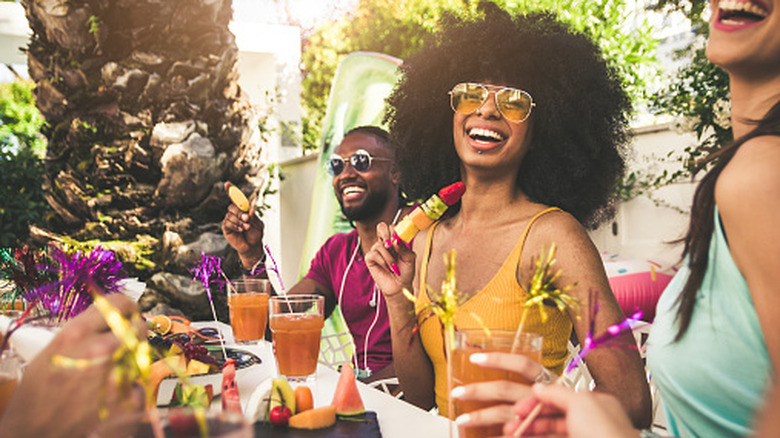 Happy people sitting around an outdoor table enjoying fruit and cocktails in a brunch-like setting