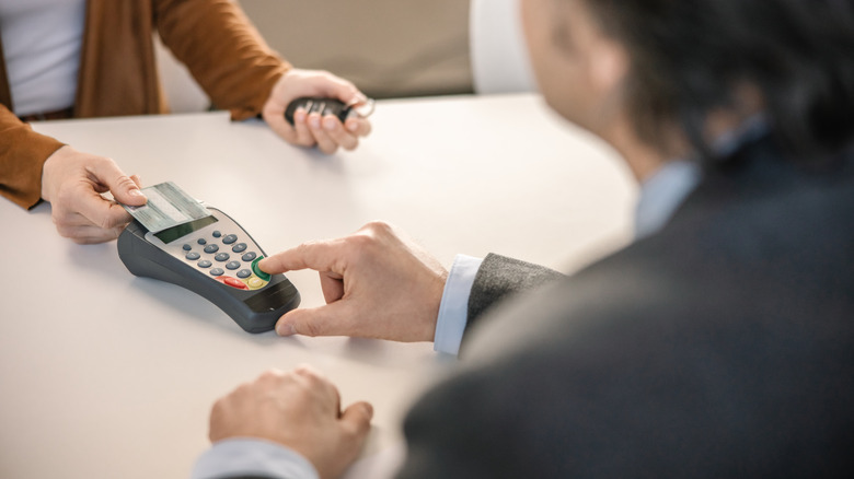 A car rental counter customer holding keys, swiping a credit card.