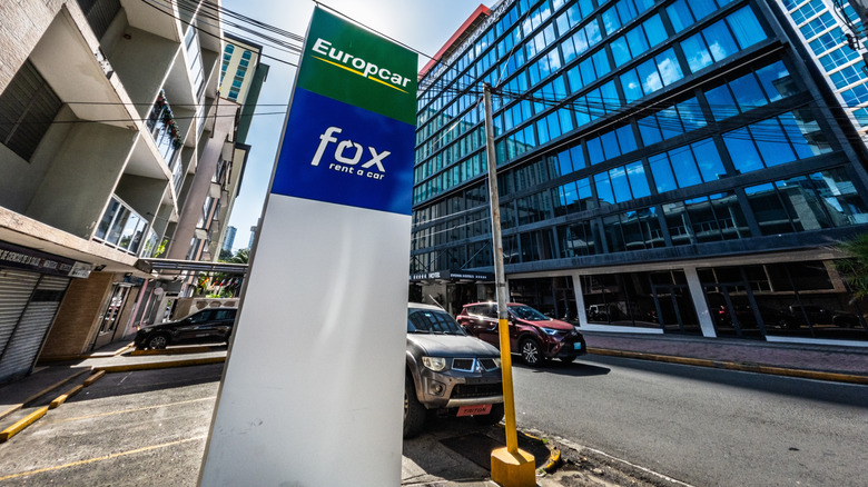 Sign for off-airport budget car rental agencies Europcar and Fox on an urban street.