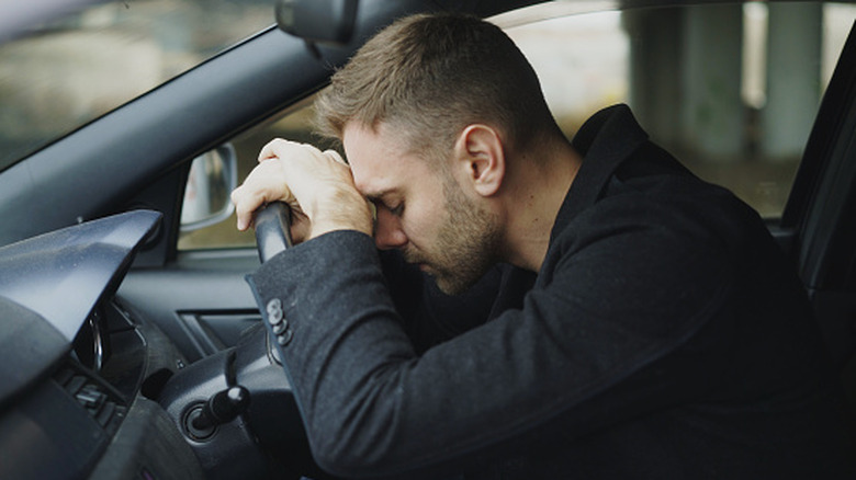 A man in despair resting his head on the steering wheel of a car.